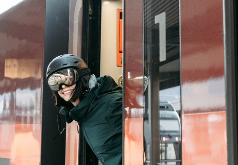 Frau mit Skihelm und Brille steigt aus Zug aus