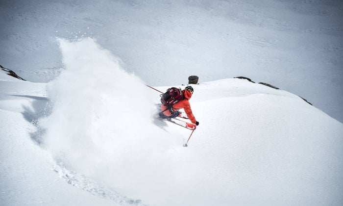 Ein Freerider fährt einen Rechtsschwung durch den kniehohen Tiefschnee